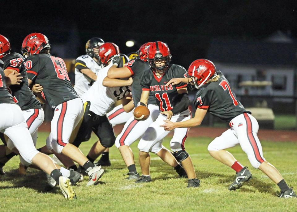 Winfield-Mt. Union quarterback Cole Milks (11) hands off to Eli Miller (7) behind the WMU offensive line in the Wolves 60-0 win over Tri County