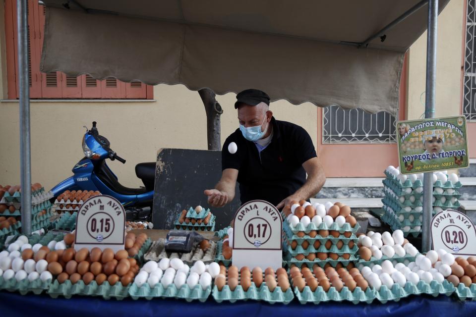 A vendor wearing a face mask against the spread of coronavirus, throws and catches an egg in the air at an open-air fruit and vegetable market in Athens, Monday, Nov. 23, 2020. Greece has seen a major resurgence of the virus after the summer, leading to dozens of deaths each day and thousands of new infections. (AP Photo/Thanassis Stavrakis)