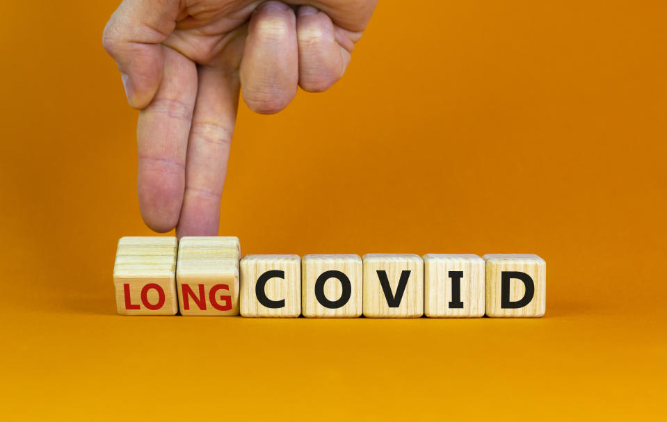 Long covid symbol. Doctor turnes wooden cubes and changes words 'covid' to 'long covid'. Beautiful orange background, copy space. Medical, covid-19 pandemic long covid concept.