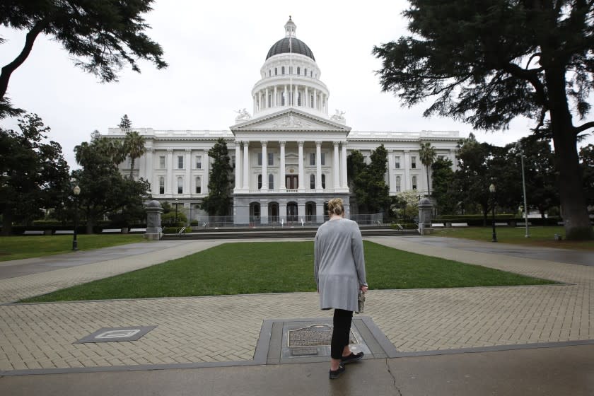 FILE - In this March 18, 2020, file photo, a woman pauses to look at the historical marker about the state Capitol in Sacramento, Calif. A veteran employee at the California state Capitol has died after contracting the coronavirus. Lawrence "Larry" Luna III died on Dec. 22, 2020, after a battle with COVID-19, according to a memo from Secretary of the Senate Erika Contreras. The 58-year-old was the automotive pool manager for the Department of General Services at the Capitol garage. (AP Photo/Rich Pedroncelli, File)