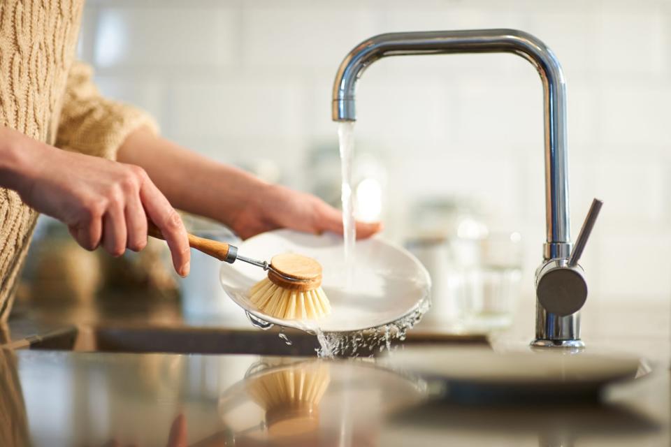 A woman uses a plastic free brush to clean dishes in a kitchen sink, close up.