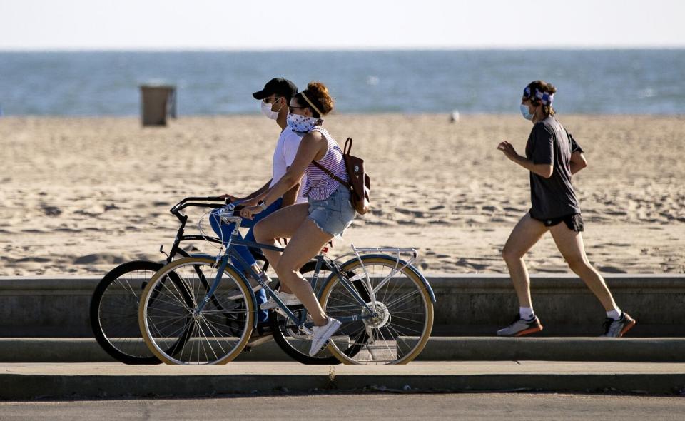 Bicyclists and a runner wear masks on a beach boardwalk