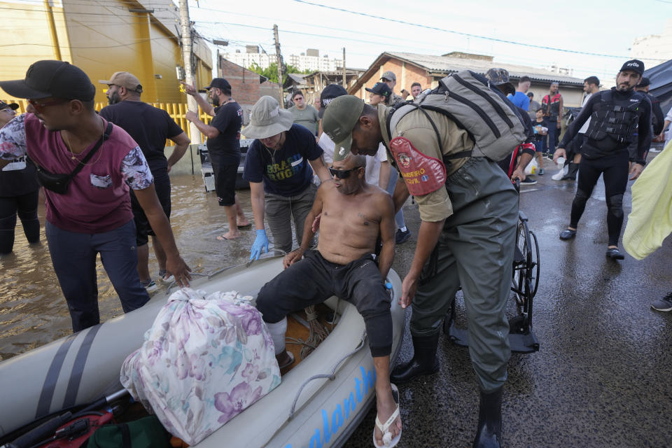 A civil firefighter helps a resident evacuated from an area flooded by heavy rains in Porto Alegre, Brazil, Tuesday, May 7, 2024. (AP Photo/Andre Penner)