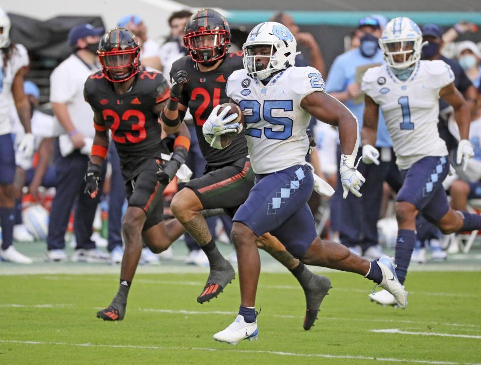 North Carolina running back Javonte Williams (25) runs the ball as Miami cornerback Te'Cory Couch (23) and Bubba Bolden (21) give chase. (Al Diaz/Miami Herald via AP)