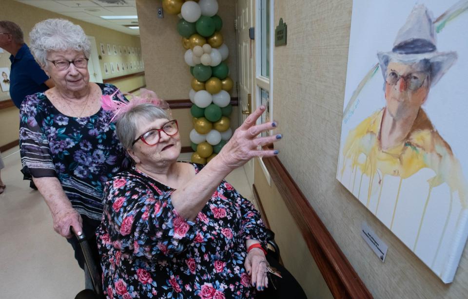 Nancy Norris, left, looks on as her sister Gail Ellingson talks about her portrait painted by local artist Nina Fritz at the Life Care Center of Pensacola on Thursday, April 25, 2024. Nearly 120 staff and resident watercolor portraits painted by Fritz are currently on display on the walls of the center.