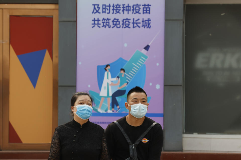 Residents wearing masks past by a vaccination site with a propaganda board displaying the slogan 