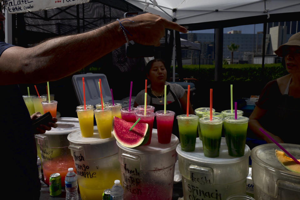 FILE - In this Sept. 21, 2018, file photo, a customer selects a drink from a vendor selling fresh juices and fruit at a farmers market in downtown Los Angeles. Avoiding single-use plastics like straws, plastic bags and water bottles is easier than it seems and can feel empowering, say those who've managed to stop using them altogether. (AP Photo/Richard Vogel, File)