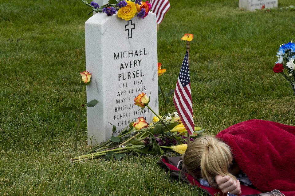 Avery Carlin, of Arlington, Va., rests by the headstone of her uncle U.S. Army Cpl. Michael Avery Pursel as she visits Section 60 at Arlington National Cemetery with her family on Memorial Day, Monday, May 29, 2023, in Arlington, Va. (AP Photo/Alex Brandon)