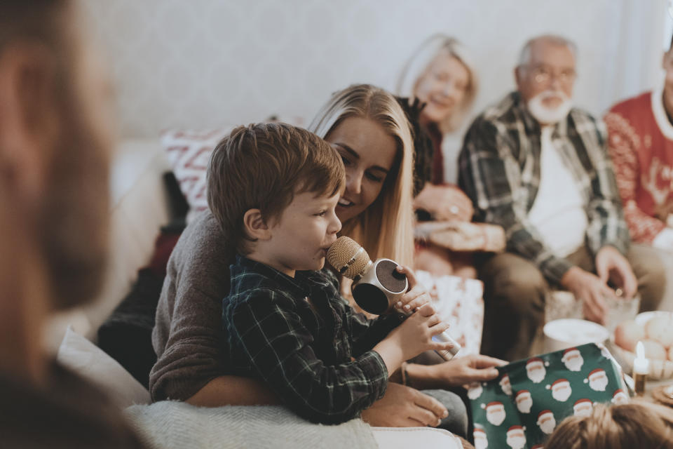 Family gathering with a child and woman holding a microphone, surrounded by adults smiling