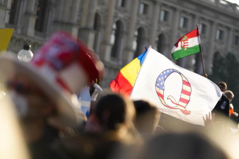 Protestors with a flag showing a 'Q' attend a demonstration against measures to battle the coronavirus pandemic in Vienna, Austria, Saturday, Nov. 20, 2021. Thousands of protesters are expected to gather in Vienna after the Austrian government announced a nationwide lockdown to contain the quickly rising coronavirus infections in the country. Poster in center reads: 'Together for Freedom'. (AP Photo/Florian Schroetter)