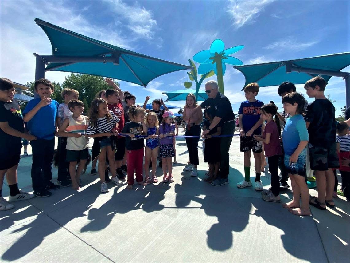 Boise Mayor Lauren McLean, center, and Boise Parks and Recreation Director Doug Holloway, center right, cut a ribbon alongside more than a dozen kids at a dedication ceremony for the new splash pad.