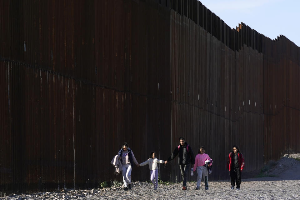 Gerston Miranda, center, and his family from Ecuador walks along the border wall as they join hundreds of migrants gathering along the border Tuesday, Dec. 5, 2023, in Lukeville, Ariz. (AP Photo/Ross D. Franklin)