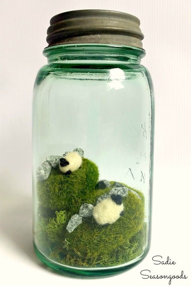 vintage mason jar made into a terrarium for a st patrick's day craft filled with moss, small rocks, and tiny felted sheep