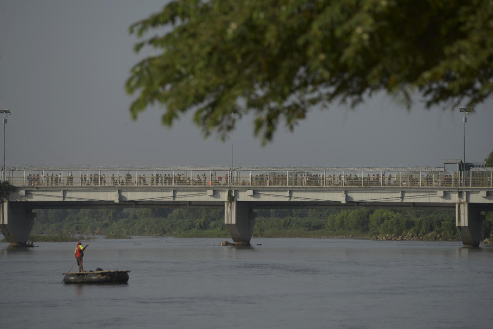 A long line of people, many commuters who typically crossed by raft, wait on the international bridge to enter Mexico from Guatemala, as an empty raft plies the Suchiate River, in Ciudad Hidalgo, Mexico, Thursday, July 4, 2019. On Thursday, migrants and local commuters crossing informally by raft were being sent back across the river by migration agents, with instructions to use the official port of entry on the adjacent bridge. (AP Photo/Idalia Rie)