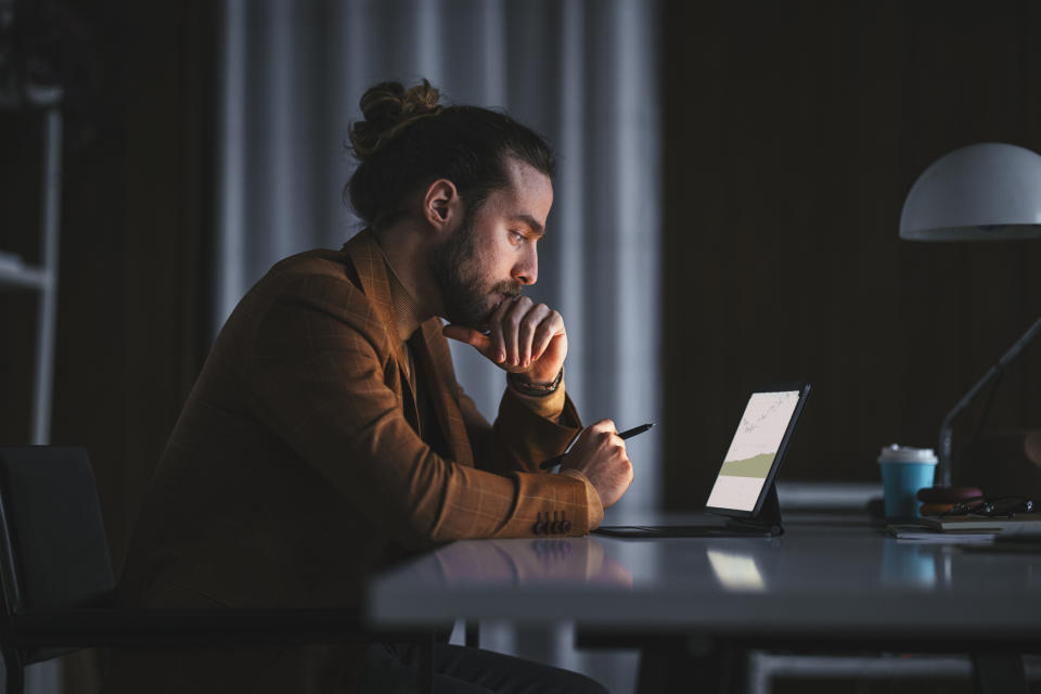 A person in a darkened room looking at stock charts on a tablet