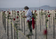 A woman places a rose in the sand on Copacabana beach in honor of 500,000 coronavirus deaths, during a protest against Brazilian President Jair Bolsonaro and his handling of the COVID-19 pandemic, in Rio de Janeiro, Brazil, Sunday, June 20, 2021. Brazil's COVID-19 death toll surpassed the milestone of 500,000 deaths on Saturday night. (AP Photo/Silvia Izquierdo)