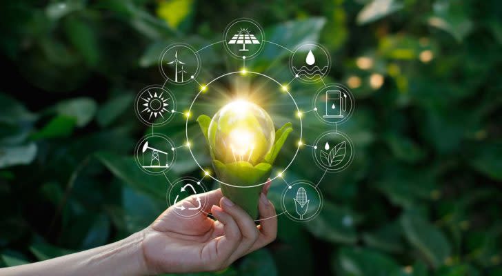 a hand holding a lightbulb on a green background to represent renewable energy stocks