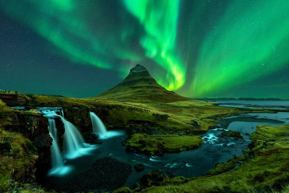 Northern lights appear on Mount Kirkjufell with the Kirkjufellfoss waterfall in Iceland.