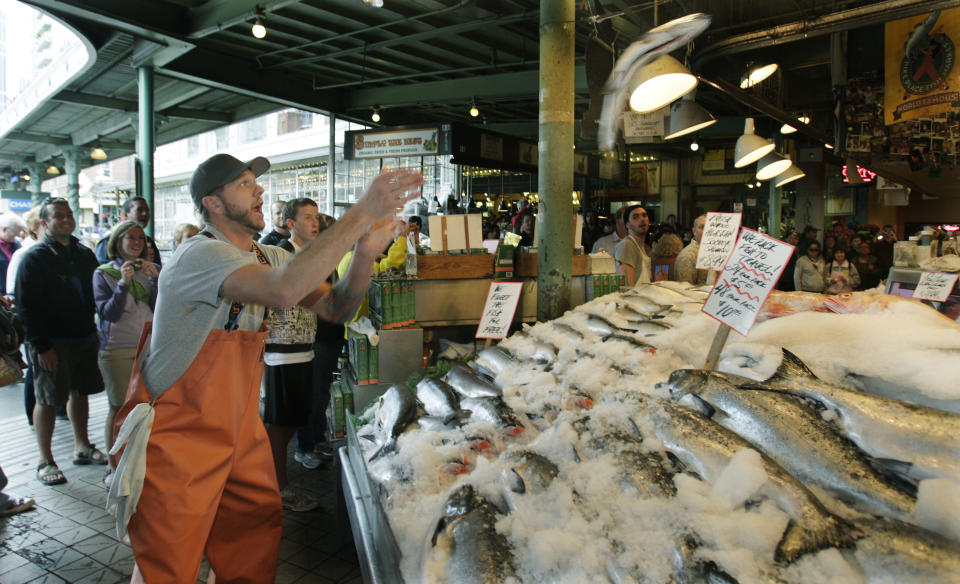 FILE - This July 11, 2009 file photo shows Justin Hall throwing a salmon to a co-worker behind the counter at Pike Place Fish, at Pike Place Market in Seattle. The market and the fish throw are a favorite and free attraction for visitors to Seattle. (AP Photo/Ted S. Warren, file)