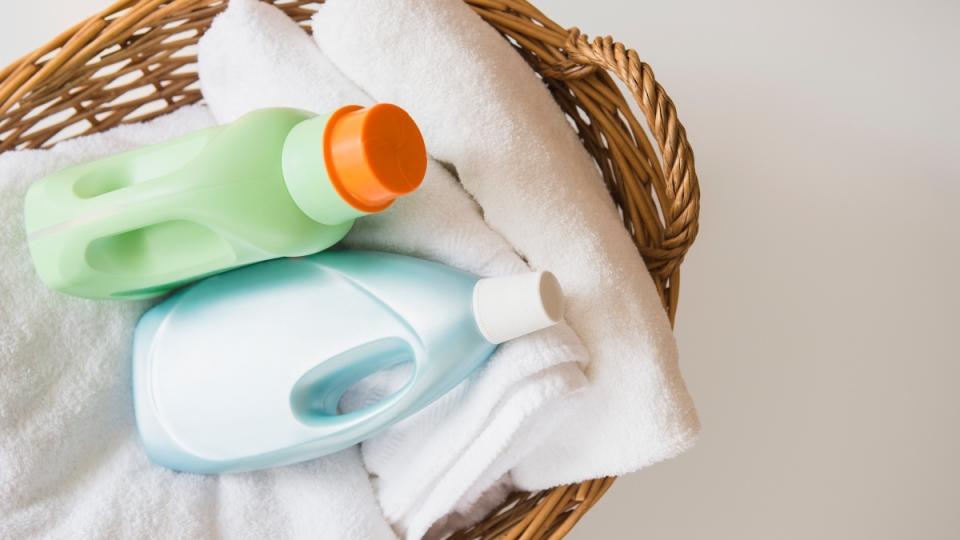 Blue and green bottles of laundry detergent in a wicker basket with white towels