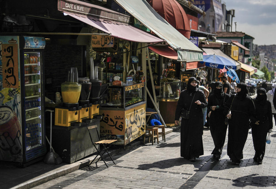 Women walk past a Syrian restaurant in an outdoor market in Fatih district of Istanbul, Turkey, Tuesday, May 23, 2023. Two opposing visions for Turkey’s future are on the ballot when voters return to the polls Sunday for a runoff presidential election, which will decide between an increasingly authoritarian incumbent President Recep Tayyip Erdogan and challenger Kemal Kilicdaroglu, who has pledged to restore democracy. (AP Photo/Khalil Hamra)