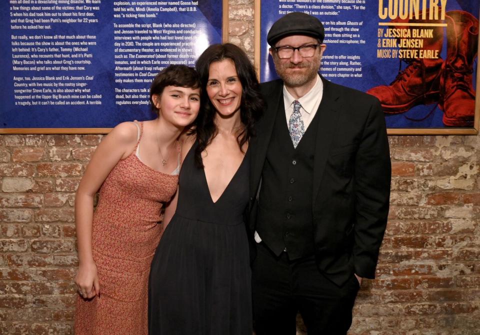 Eric Jensen in a dark suit is posing with his wife Jessica Blank in a black dress and daughter Sadie in an orange dress