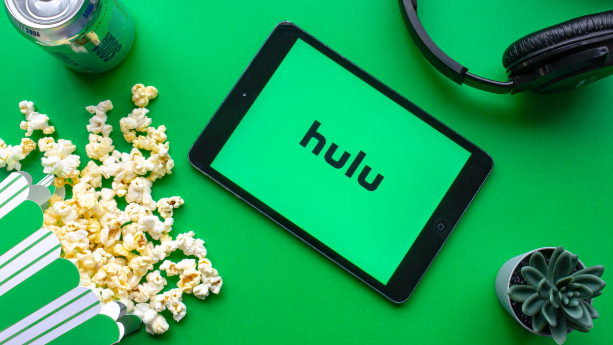  An iPad with the Hulu logo on the screen on a green background with popcorn and headphones. 