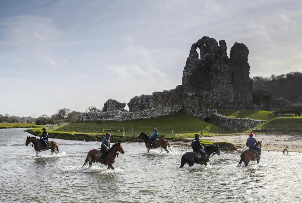 Horses from Christian Williams' stables exercise in the river backdropped by Ogmore Castle in Glamorgan, South Wales, Saturday March 21, 2020. All horse racing fixtures in Great Britain have been suspended because of the coronavirus outbreak. For some people the COVID-19 coronavirus causes mild or moderate symptoms, but for others it causes severe illness. (David Davies / PA via AP)