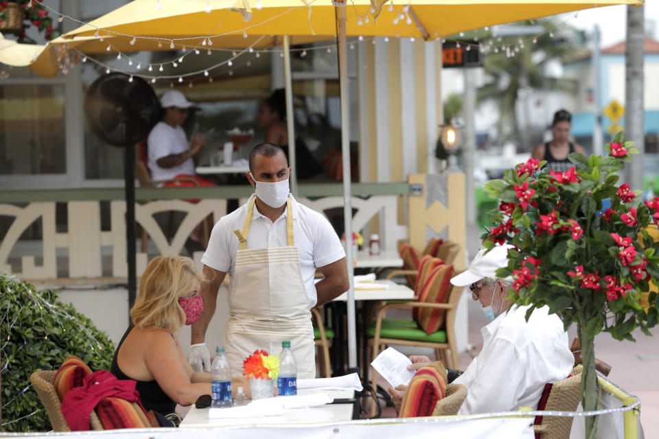 Jeffrey Holinka wears a protective face mask as he waits to receive an order at the On Ocean 7 Cafe along Ocean Drive in Miami Beach, Fla. during the new coronavirus pandemic, Wednesday, May 27, 2020. Ocean Drive was closed to traffic as restaurants in Miami Beach reopened Wednesday after being closed to mitigate the spread of the coronavirus. (AP Photo/Lynne Sladky)