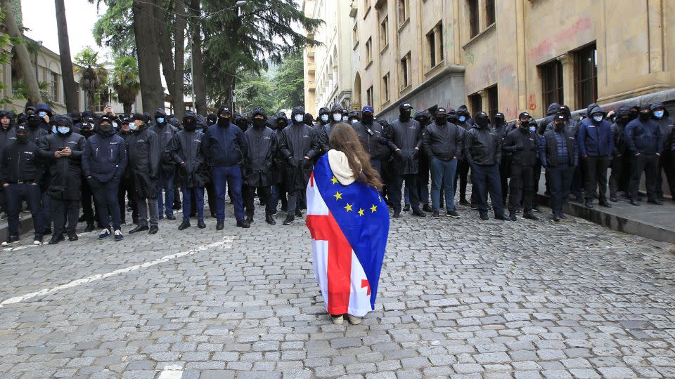 A protester, draped with Georgian national and European Union flags, stands before police officers blocking the way to the country's parliament building on Tuesday. - Shakh Aivazov/AP
