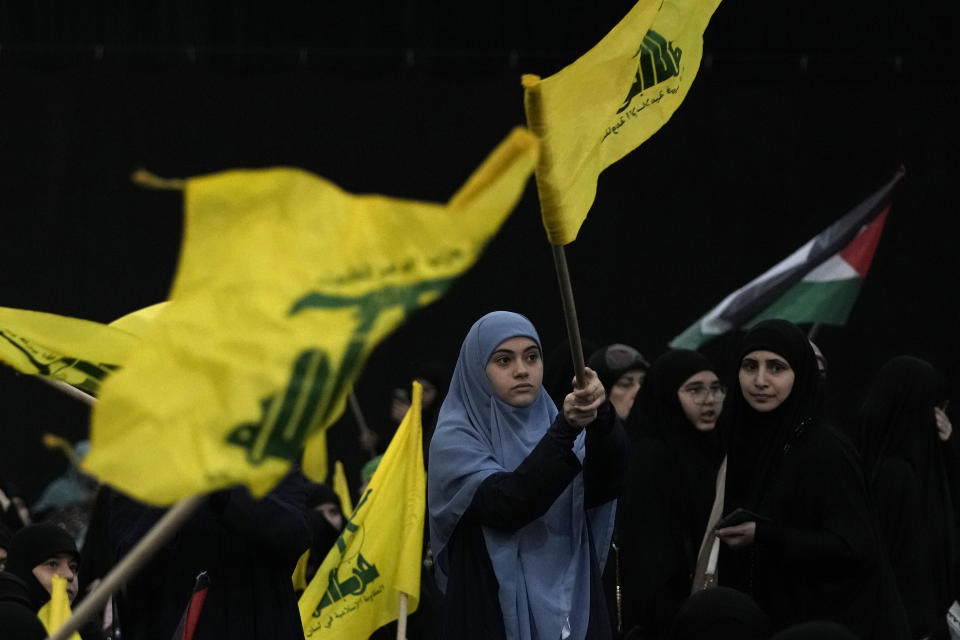 Hezbollah supporters wave Hezbollah and Palestinian flags as Hezbollah leader Sayyed Hassan Nasrallah speaks via a video link during a ceremony to commemorate the death of the Iranian Revolutionary Guard Gen. Mohammad Reza Zahedi, and six officers, who were killed by an Israeli airstrike that demolished Iran's consulate in Syria last Monday, in the southern suburbs of Beirut, Lebanon, Monday, April 8, 2024. Nasrallah paid tribute to Zahedi, who spent 12 years of his career as a top general at the Iranian Revolutionary Guards elite Quds Force with Hezbollah. The Hezbollah leader said he played a key role in strengthening and empowering the group which fought several wars with Israel, and has become Iran's key proxy in the region. (AP Photo/Hassan Ammar)