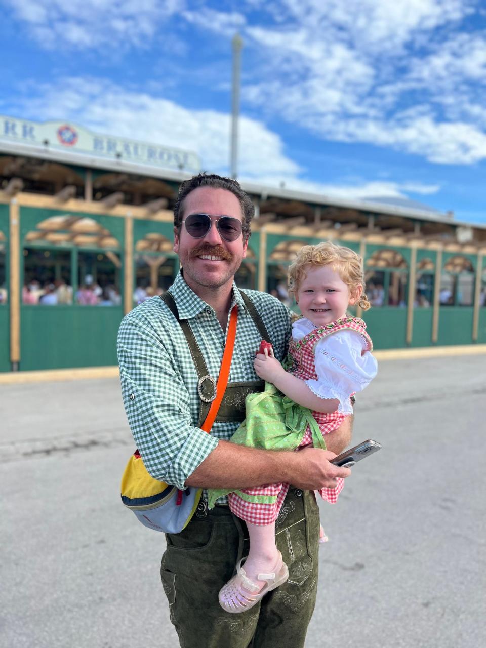 A man holds his daughter on his hip. They both wear gingham clothes.