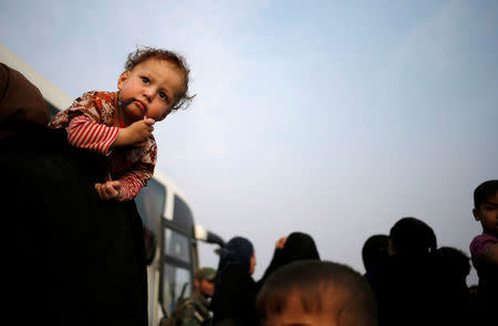 An internally displaced woman carries her child into a bus near Hassan Sham, east of Mosul, Iraq October 25, 2016. REUTERS/Goran Tomasevic