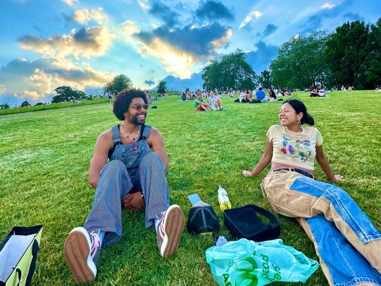 malik and a friend sitting on the grass in a park in london with a blue sky behind them