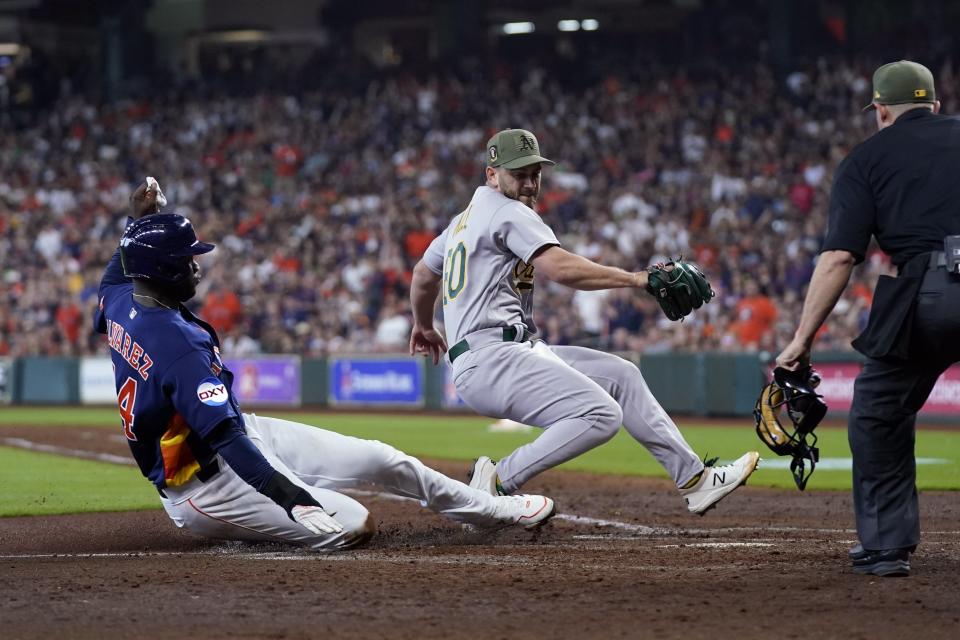 Houston Astros' Yordan Alvarez, left, scores as Oakland Athletics relief pitcher Sam Moll, right, covers home plate after throwing a wild pitch during the sixth inning of a baseball game Sunday, May 21, 2023, in Houston. (AP Photo/David J. Phillip)