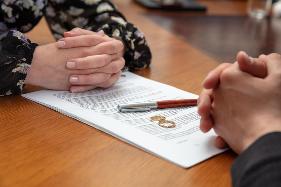 A couple signs a divorce document and sets their wedding rings down on the paperwork