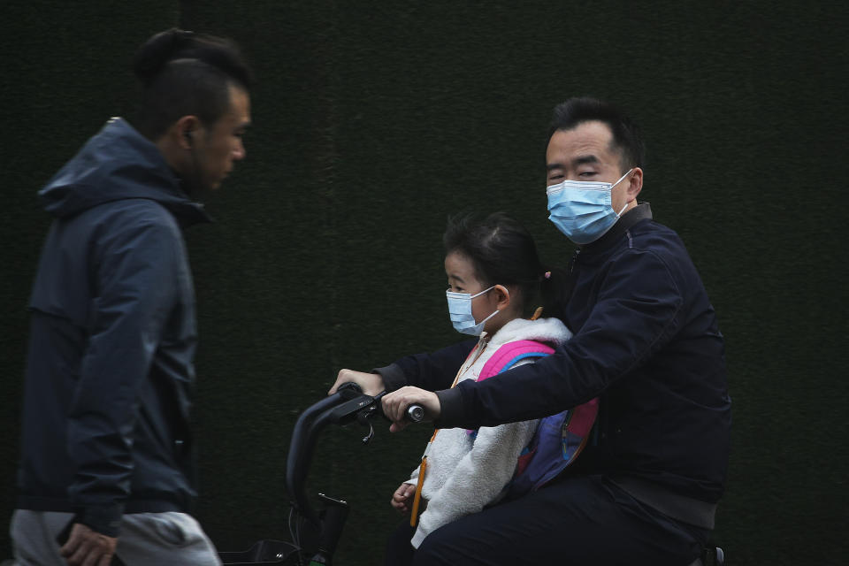 A man and a child, both wearing face masks to help curb the spread of the coronavirus ride on an electric-powered scooter in Beijing, Monday, Oct. 26, 2020. Schools and kindergartens have been suspended and communities are on lockdown in Kashgar, a city in China's northwest Xinjiang region, after more than 130 asymptomatic cases of the coronavirus were discovered. (AP Photo/Andy Wong)