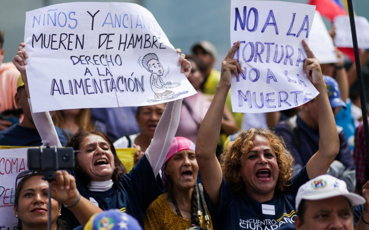 A Venezuelan opposition supporter holds up a a sign saying that children and old people are dying of hunger - AFP