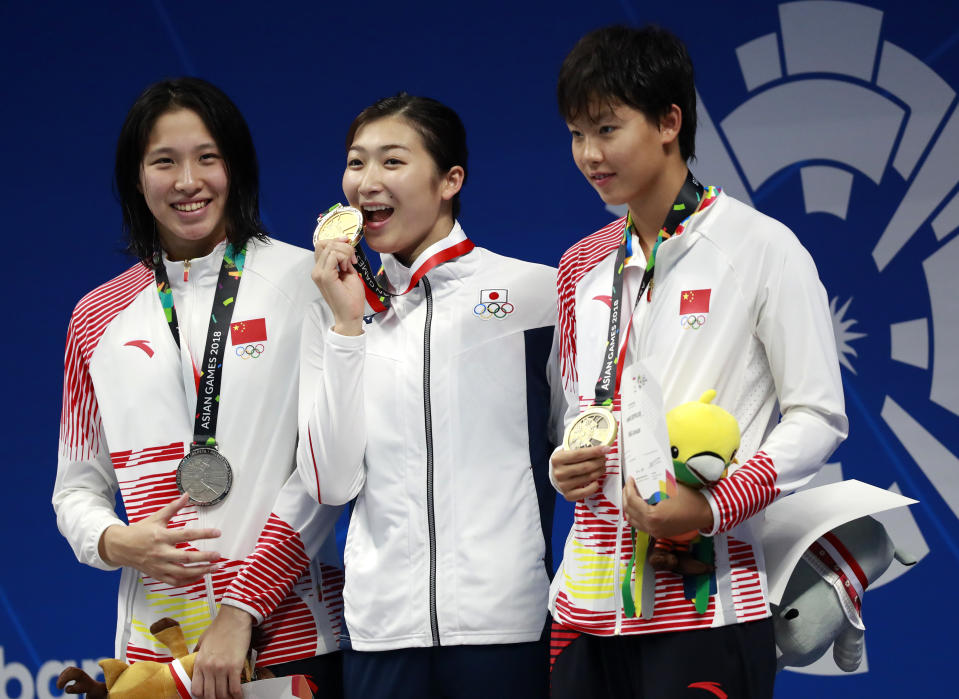 Women's 100m freestyle gold medalist Japan's Rikako Ikee, centre, stands with silver medalist China's Zhu Menghui, left, and bronze medalist Yang Junxuan on the podium during the swimming competition at the 18th Asian Games in Jakarta, Indonesia, Monday, Aug. 20, 2018. (AP Photo/Bernat Armangue)