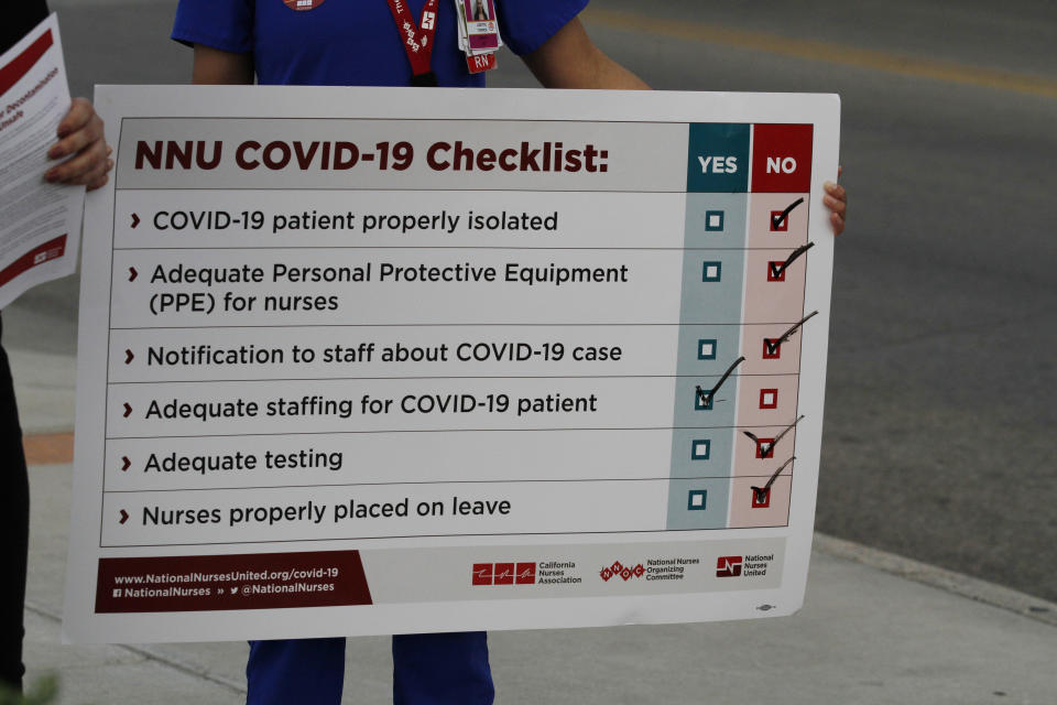 Lizette Torres holds a sign while fellow nurse and union member Tishna Soto, speaks to reporters as the prepare a small protest outside their work at the Las Palmas Del Sol Medical Center Wednesday, April 1, 2020, in El Paso, Texas. Torres and Soto are members of National Nurses United, and were joined in calling for increased transparency and safety measures by members in other states. Tensions are running high at U.S. hospitals as medical systems in New York, Washington and Louisiana are shouldering an influx of patients with COVID-19 and workers lack protective gear. (AP Photo/Cedar Attanasio)