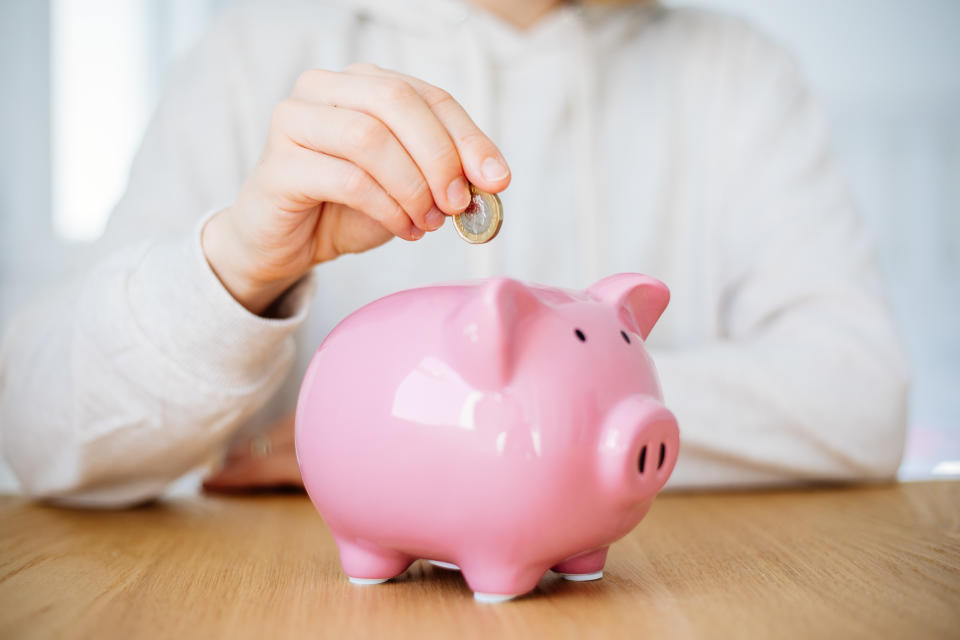 Woman's hand putting a silver coin into a pig to save money