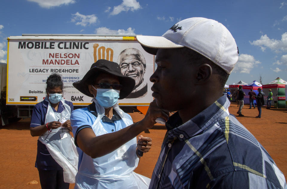 A health worker checks the temperature of a man queueing on a soccer field to be screened and tested for COVID-19 at Lenasia South, south Johannesburg, South Africa, Tuesday, April 21, 2020, during a campaign aimed to combat the spread of Coronavirus. (AP Photo/Themba Hadebe)