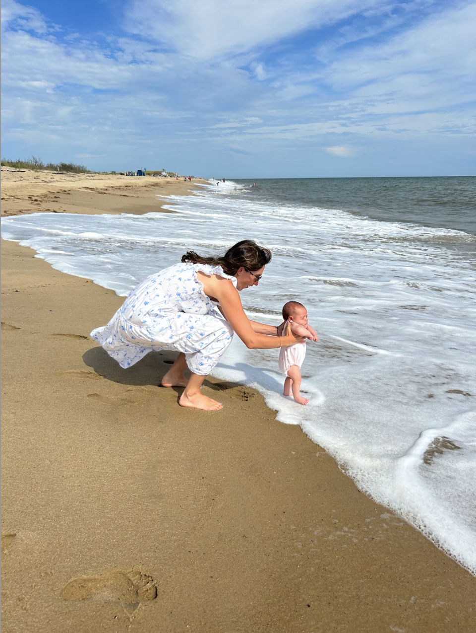 Hannah holding her daughter's feet in the water at the beach
