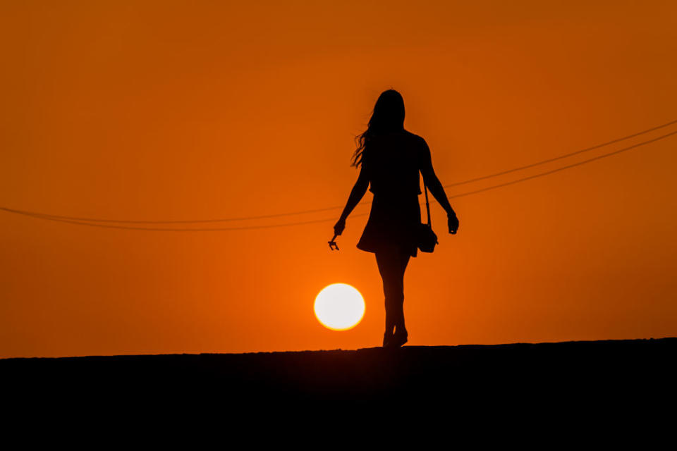 The silhouette of a woman walking on a road as the sun sets. Source: Getty