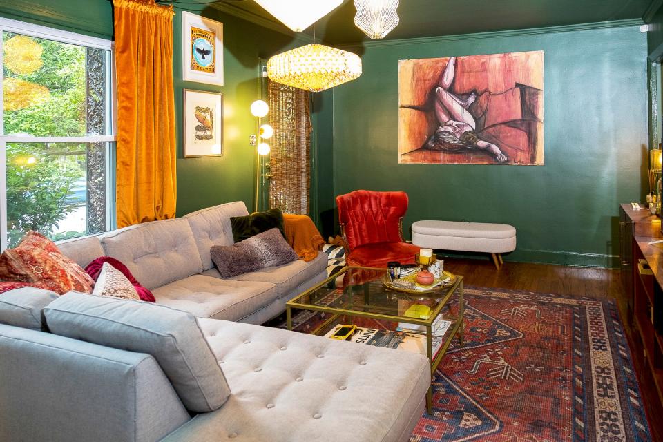 The living room features an eclectic mix of furniture and art. The walls and the ceiling are painted a very dark green tone to give a different mood to the room from the rest of the house.
