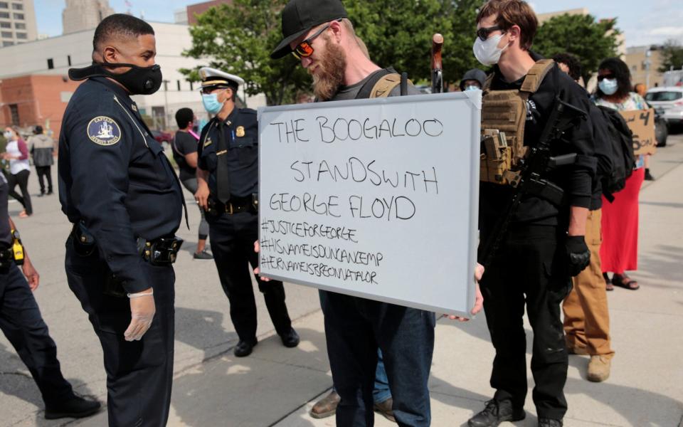 A Detroit Police officer reads a "The Boogaloo stands with George Floyd" sign held by an armed man during a rally against the death in Minneapolis police custody of George Floyd, in Detroit, Michigan, U.S. May 30, 2020. - Rebecca Cook/Reuters