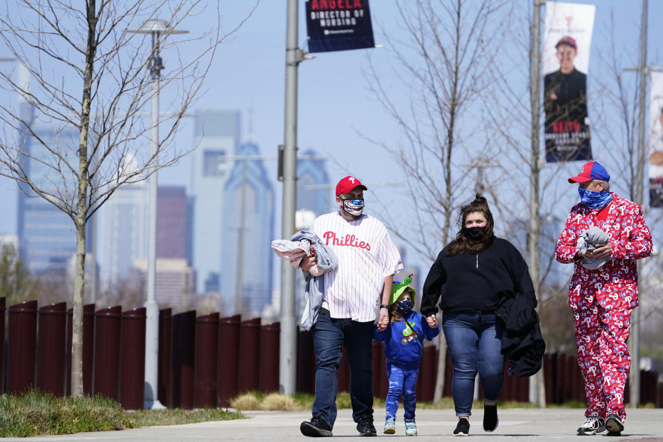 Fans walk outside Citizens Bank Park before an opening day baseball game between the Philadelphia Phillies and the Atlanta Braves, Thursday, April 1, 2021, in Philadelphia. The U.S. moved closer Thursday toward vaccinating 100 million Americans in a race against an uptick in COVID-19 cases that is fueling fears of another nationwide surge just as the major league baseball season starts and thousands of fans return to stadiums. (AP Photo/Matt Slocum)