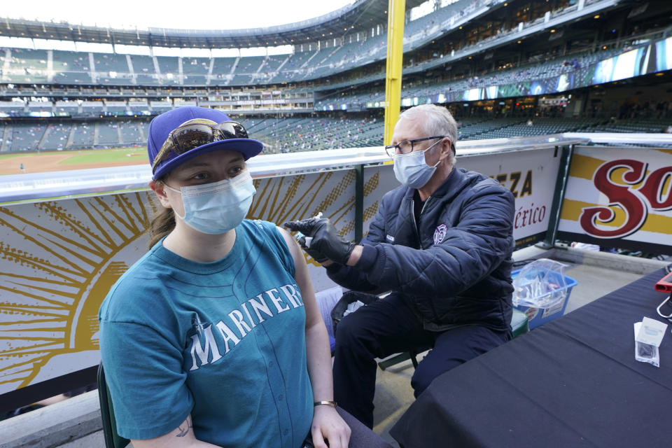 Bill Allemann, right, an EMT and firefighter with the Seattle Fire Dept., gives a Johnson & Johnson COVID-19 vaccine shot to a Seattle Mariners fan, Tuesday, May 4, 2021, during a clinic held at T-Mobile Park before a baseball game between the Mariners and the Baltimore Orioles in Seattle. The Mariners will be offering free COVID-19 vaccines to eligible fans at three locations in the ballpark during upcoming home games. (AP Photo/Ted S. Warren)