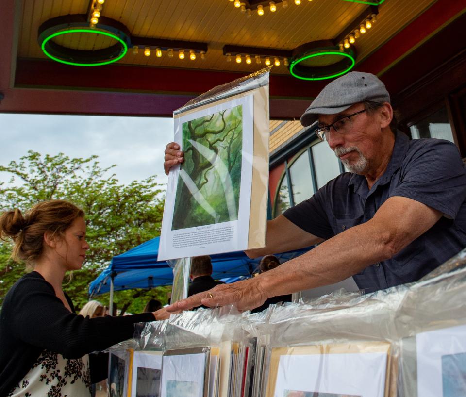 Jon Fuchs organizes his watercolor paintings as Andrea Lantz, left, searches for a print at his vendor table under the awning of the Alhambra Theater during First Friday in Haynie’s Corner Arts District in Evansville, Ind., Friday, May 5, 2023.