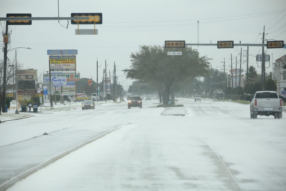 Vehicles drive down a road dusted with snow, with traffic lights out.